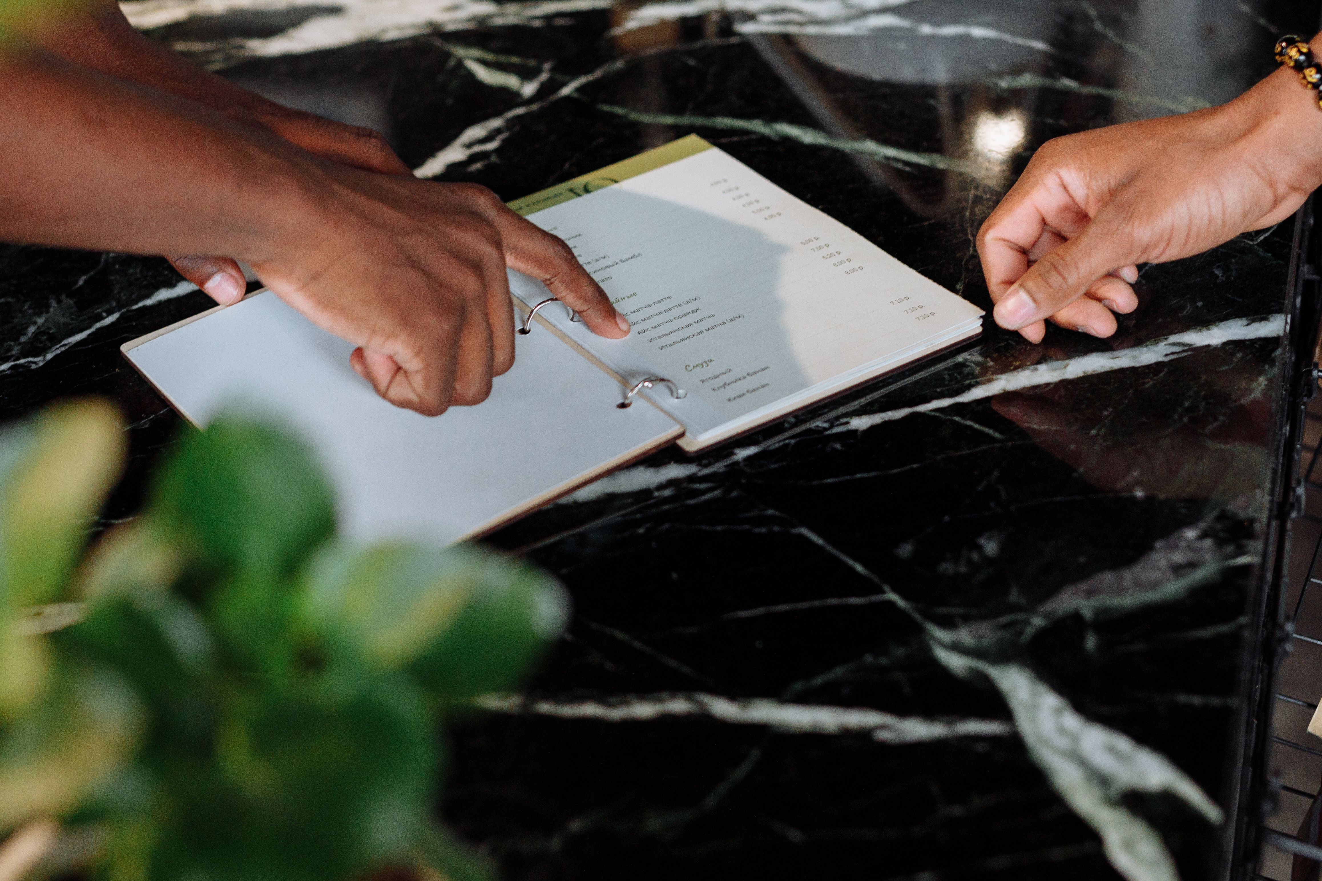 Hands reviewing a restaurant menu on a counter, illustrating menu planning and design